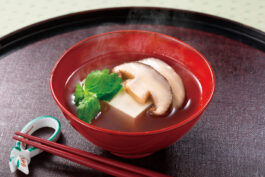 A bowl of broth with sliced shiitake mushrooms.