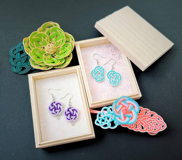 Purple and teal mizuhiki knot earrings nestled in wooden gift boxes, alongside a green floral ornament and coral hair accessory — handmade in RESOBOX's mizuhiki class in New York