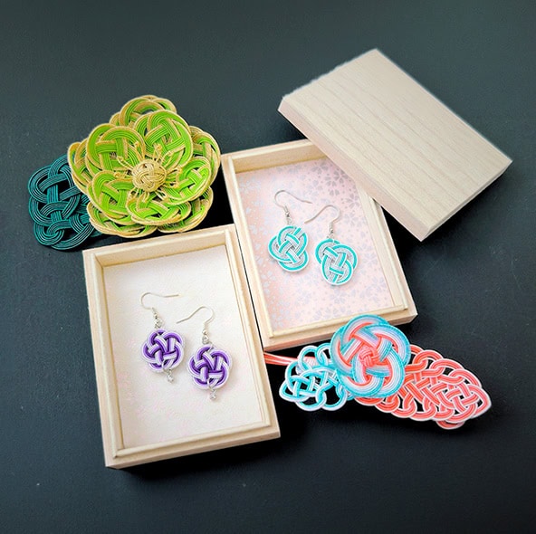 Purple and teal mizuhiki knot earrings nestled in wooden gift boxes, alongside a green floral ornament and coral hair accessory — handmade in RESOBOX's mizuhiki class in New York