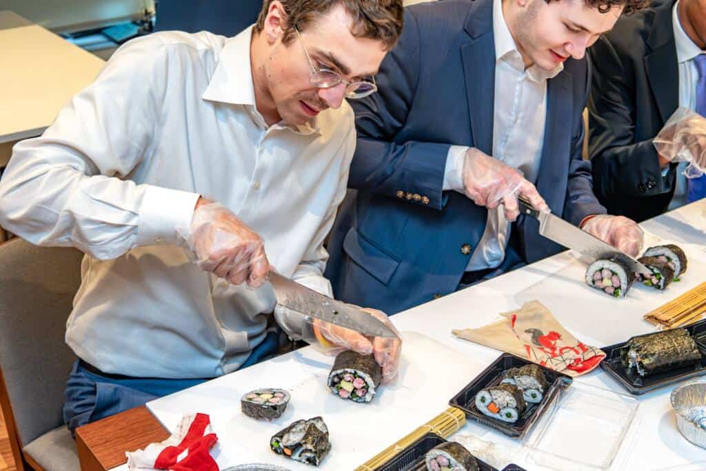 Business professionals in suits slicing decorative kazari maki zushi rolls during a private sushi workshop at RESOBOX in New York