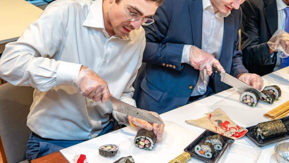 Business professionals in suits slicing decorative kazari maki zushi rolls during a private sushi workshop at RESOBOX in New York