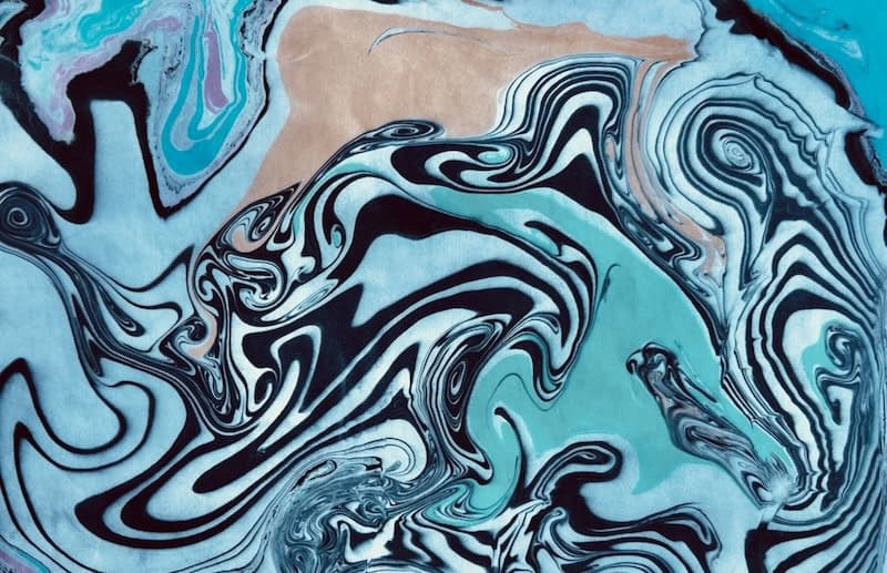 Swirling patterns of teal, black, and cream ink float across paper in the ancient Japanese art of suminagashi, practiced in a marbling class at RESOBOX in New York's East Village