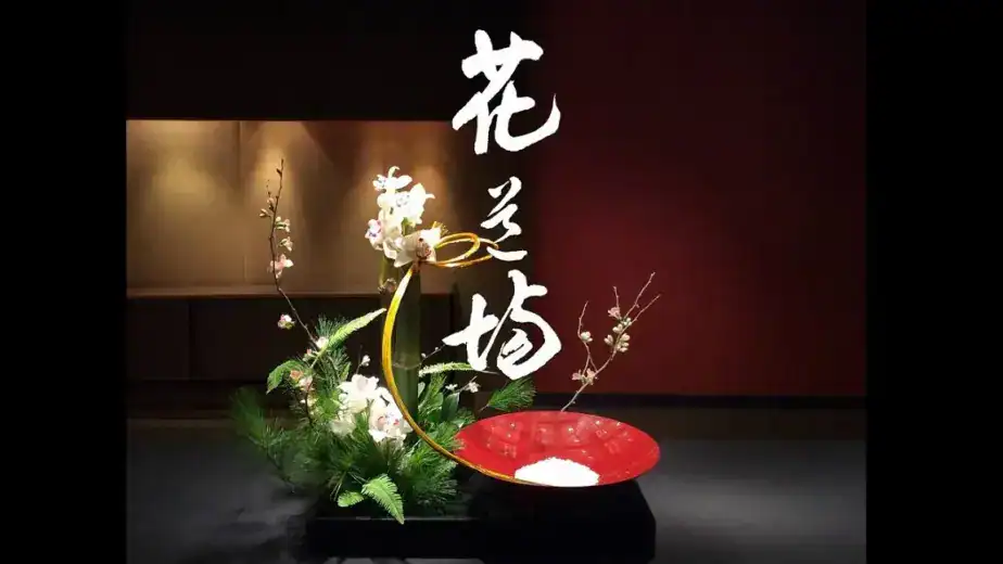 A formal Japanese ikebana new year arrangement featuring white orchids, curved bamboo, pine, and plum blossoms in a red lacquer dish — displayed at RESOBOX in New York