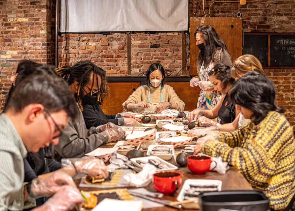 A group of participants rolling sushi together around a long table during a hands-on class at RESOBOX in New York’s East Village