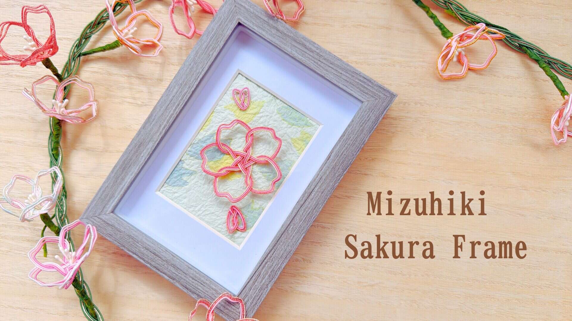 A handcrafted mizuhiki sakura cherry blossom framed on Japanese washi paper, surrounded by delicate cord flower decorations — made in RESOBOX's Mizuhiki Sakura Frame class in New York