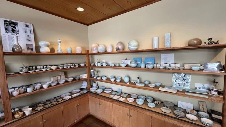 Japanese ceramic pottery collection displayed on wooden shelves, featuring traditional Hagi ware bowls, plates, and vessels in various glazes and colors - artisanal pottery from Hagi, Yamaguchi Prefecture