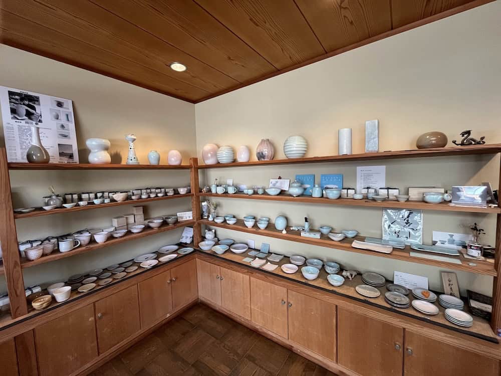 Japanese ceramic pottery collection displayed on wooden shelves, featuring traditional Hagi ware bowls, plates, and vessels in various glazes and colors - artisanal pottery from Hagi, Yamaguchi Prefecture
