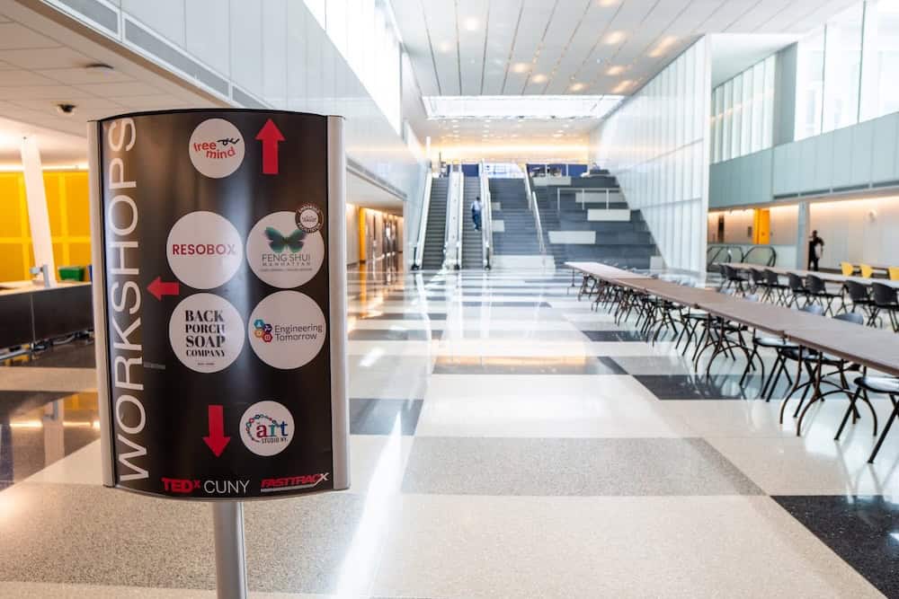 Cylindrical workshop directory sign at TEDxCUNY event displaying RESOB­OX and multiple Japanese cultural partners including sumi-e painting and traditional arts workshops in modern venue hallway