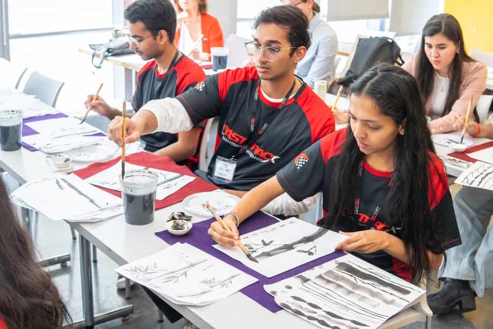 Multiple participants actively practicing traditional sumi-e ink painting with natural brushes during TEDxCUNY workshop, demonstrating hands-on engagement with Japanese artistic techniques and cultural education