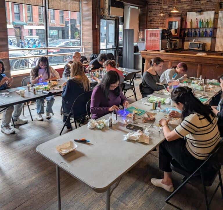 A full room of participants engaged in a miniature food-making workshop at RESOBOX, seated at tables with craft supplies in a cozy NYC venue
