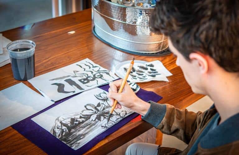 Student holding a brush and painting flowers in sumi ink