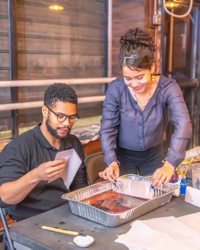 Two students lifting a marbled print from the water tray