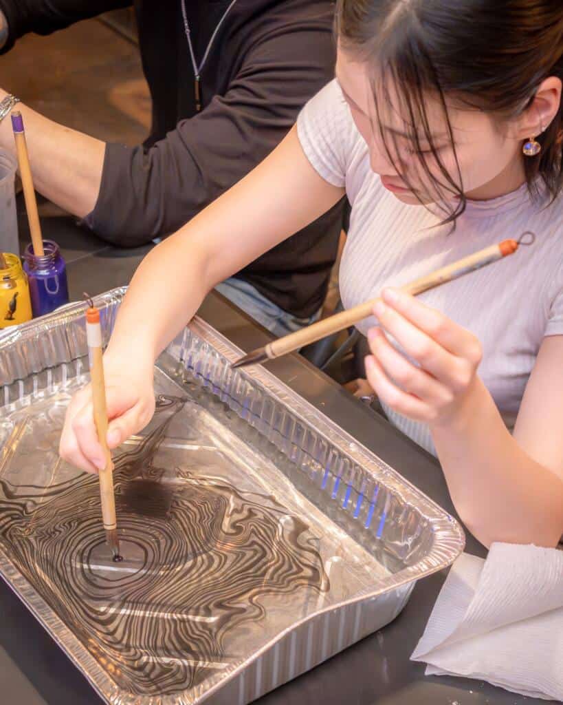 Student swirling ink on the surface of water with a brush