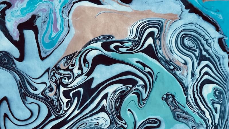A close-up of a suminagashi Japanese ink marbling artwork featuring flowing swirls of teal, black, white, and sand tones, created in a suminagashi class at RESOBOX in New York