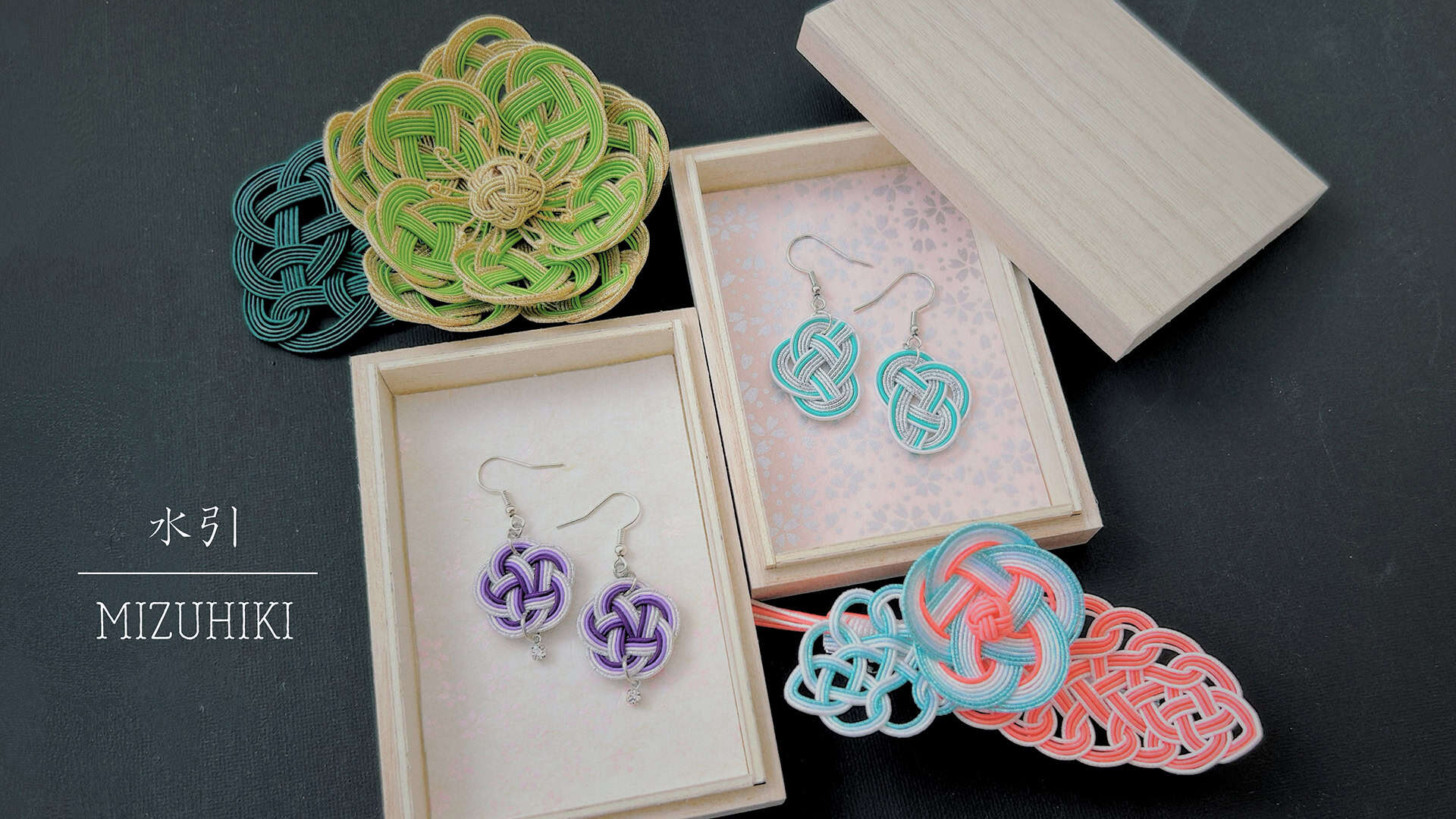 Handcrafted mizuhiki earrings and decorative knot ornaments displayed in wooden gift boxes — a traditional Japanese cord-tying art taught at RESOBOX in New Yor