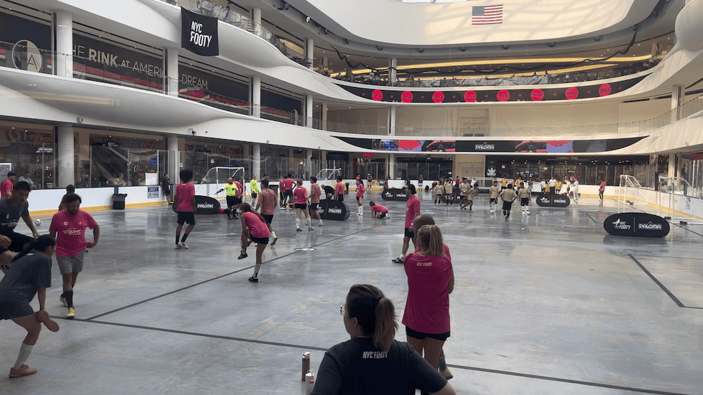 NYC Footy Cup of Dreams indoor 5v5 soccer tournament at American Dream mall, with amateur soccer players in maroon and black team jerseys competing on professional ice rink converted to soccer field, featuring multiple teams and