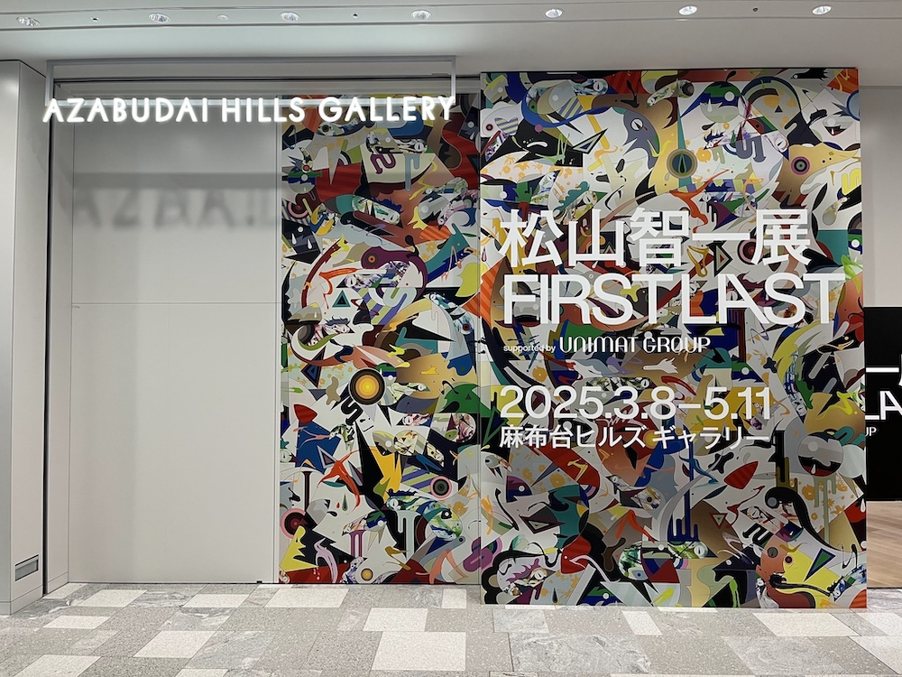 東京麻布台ヒルズの現代美術ギャラリーエントランスに掲げられた「松山智一展 FIRST LAST」の展示看板。カラフルなポップアート表現が特徴的で、ニューヨークを拠点とする現代美術家・松山智一の作品展覧会を告知している。白を基調とした高級ギャラリー空間に、極彩色の抽象的デザインが映える
