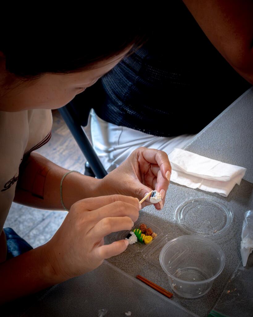 A workshop participant placing a miniature onigiri into a clay bento box