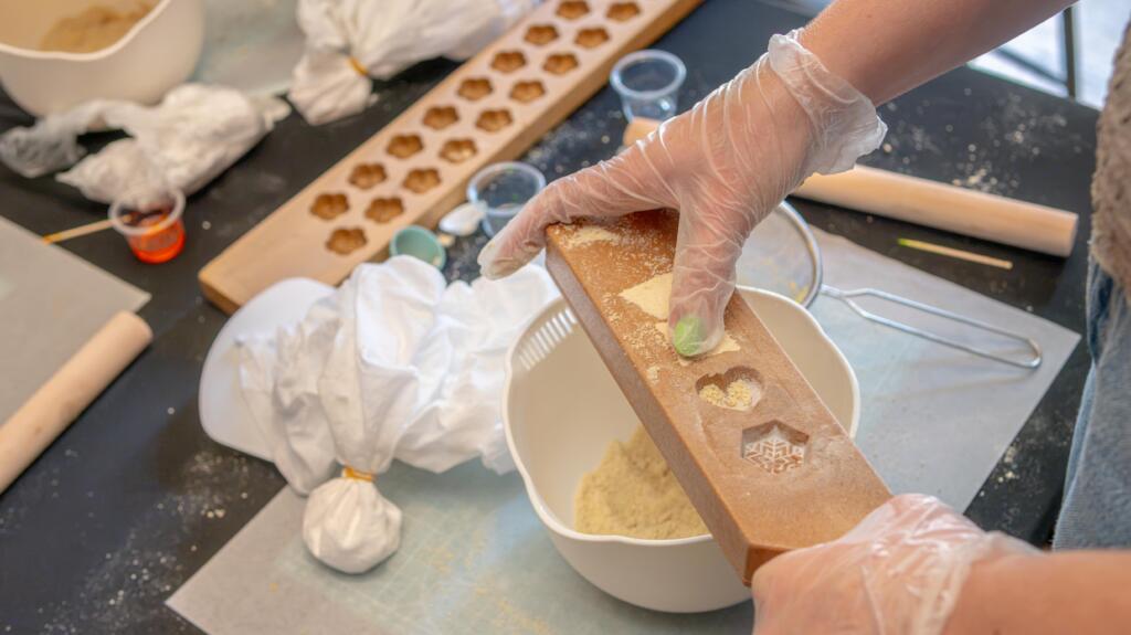 Gloved hands packing damp wasanbon sugar into a carved wooden kashigata mold