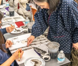 A sumi-e instructor pointing out brushwork details on a student's bamboo ink painting during a hands-on class at Columbia University