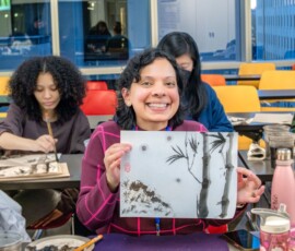 A smiling student proudly holding up her completed sumi-e ink painting of bamboo and mountains during a Japanese ink wash painting class at Columbia University
