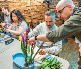 Participants placing tulips and purple liatris into a kenzan holder in a blue suiban dish during a hands-on ikebana flower arrangement class