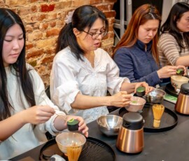 A row of participants scooping matcha powder into chawan bowls during a hands-on Japanese tea ceremony class at RESOBOX