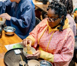 A participant carefully whisking matcha with a bamboo chasen in a chawan bowl during a hands-on Japanese tea ceremony class