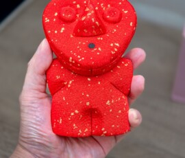 A handmade red and gold kimekomi doll in the shape of a bear, held in a hand during a kimekomi doll-making class