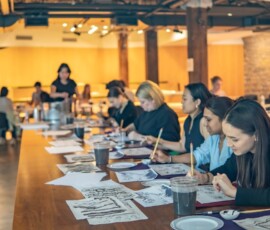 A full room of participants focused on their sumi-e ink paintings along a long wooden table at a RESOBOX Japanese ink wash painting class