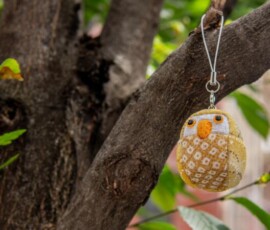 A handmade yellow kimekomi owl doll charm hanging from a tree branch, crafted with patterned chirimen fabric