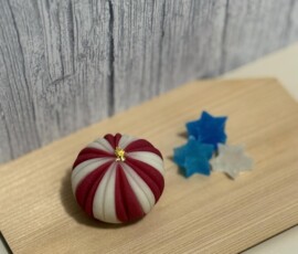 A handmade nerikiri wagashi with red and white striped pattern and gold center, displayed on a wooden board alongside small blue and white star-shaped confections