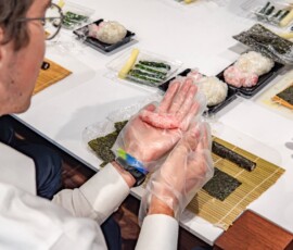 A participant shaping a pink rice filling by hand over nori on a bamboo rolling mat during a kazari maki zushi workshop