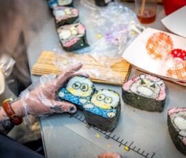 Close-up of hands arranging freshly made kazari maki zushi rolls with blue and pink character faces on a cutting mat