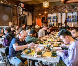 A packed kazari maki zushi workshop at RESOBOX, with a large group of participants rolling decorative sushi along long tables in a brick-walled East Village venue