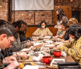 A group of participants rolling decorative sushi at a kazari maki zushi class at RESOBOX, guided by an instructor in a brick-walled East Village space